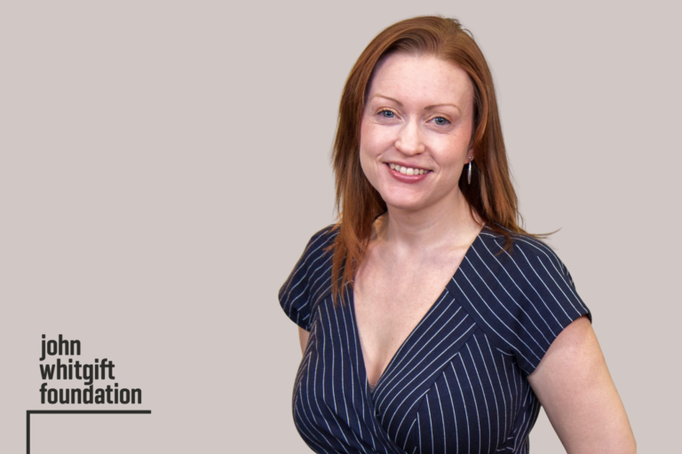 Becky is smiling. She is wearing a dark blue dress.