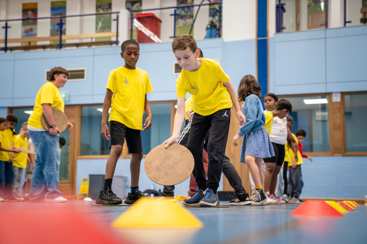 Pupils wearing yellow Community Summer School t-shirts take part in an activity in a sports hall